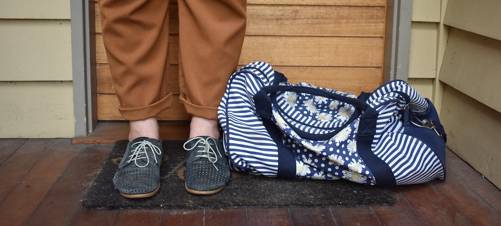 Close up of feet at doorway with bag