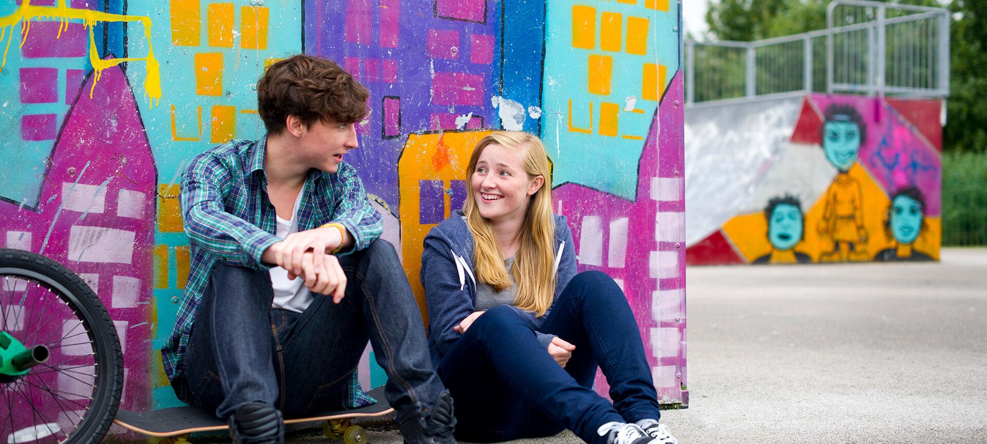 Two young people in front of graffiti wall