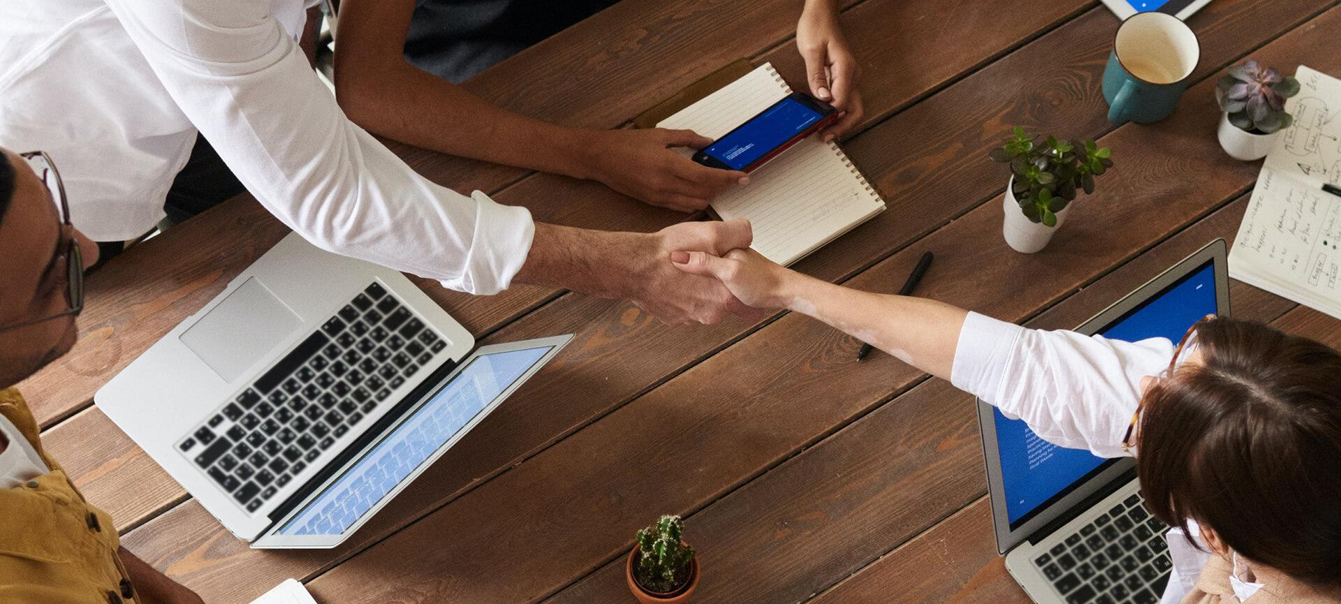 Handshake over desk with laptops