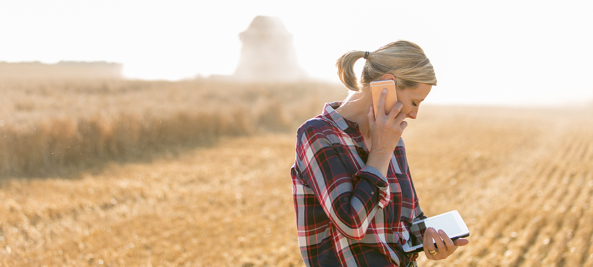 Woman standing in dry field looking at ipad and speaking on mobile phone