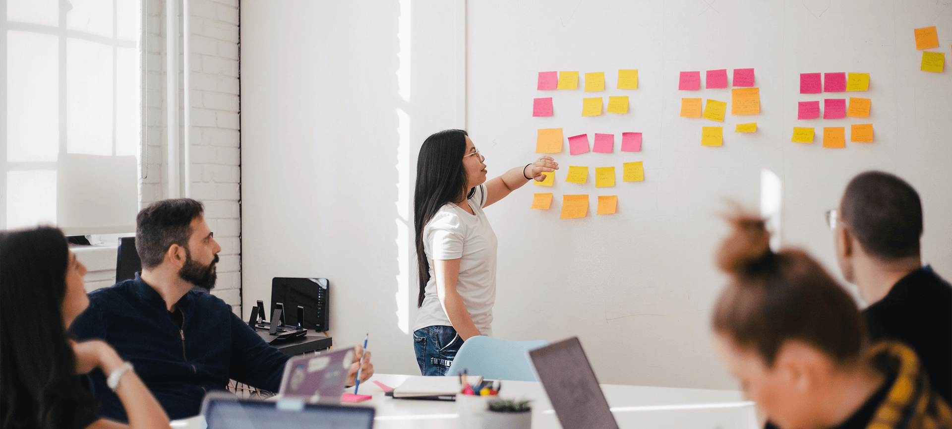 Staff with laptops looking at a woman pointing to postits