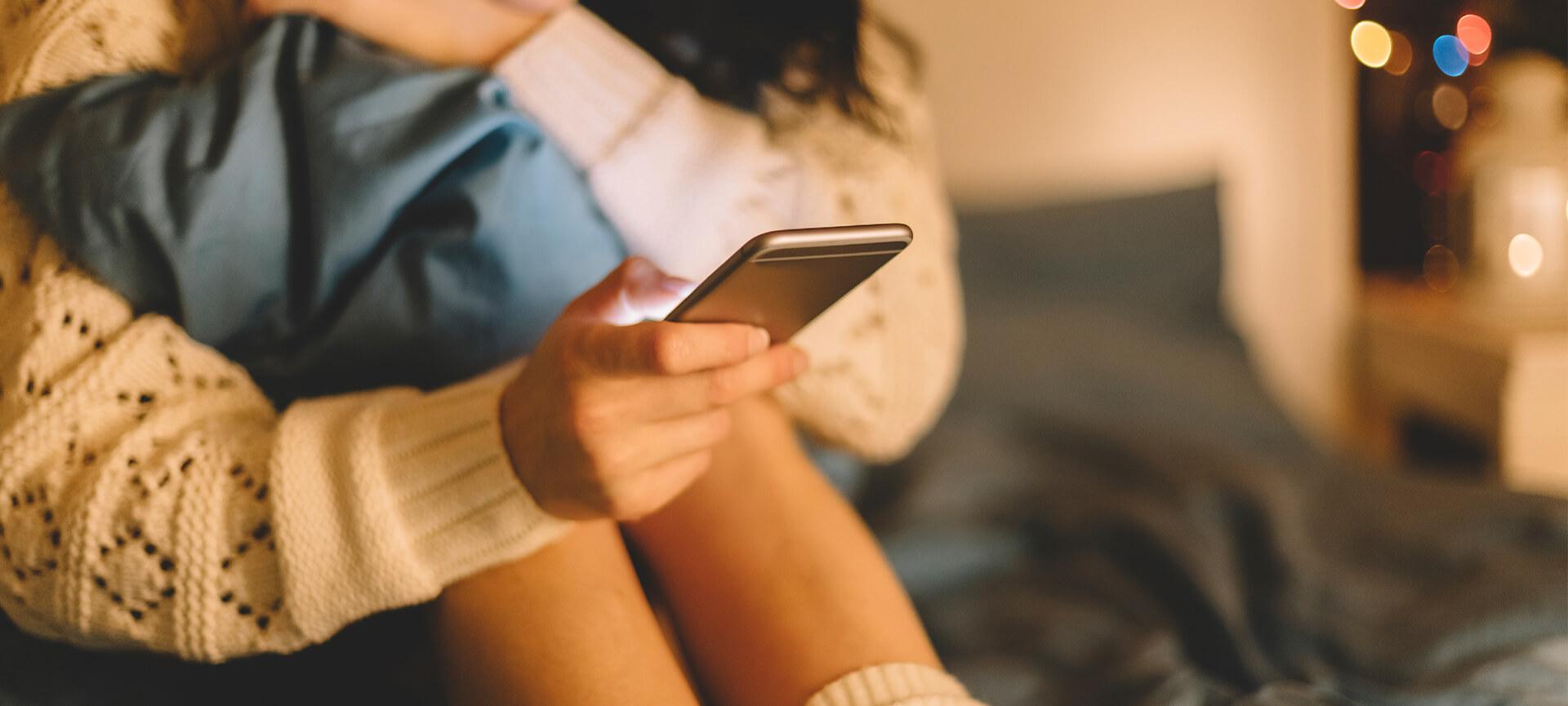 Close up of girl looking at phone sitting on her bed