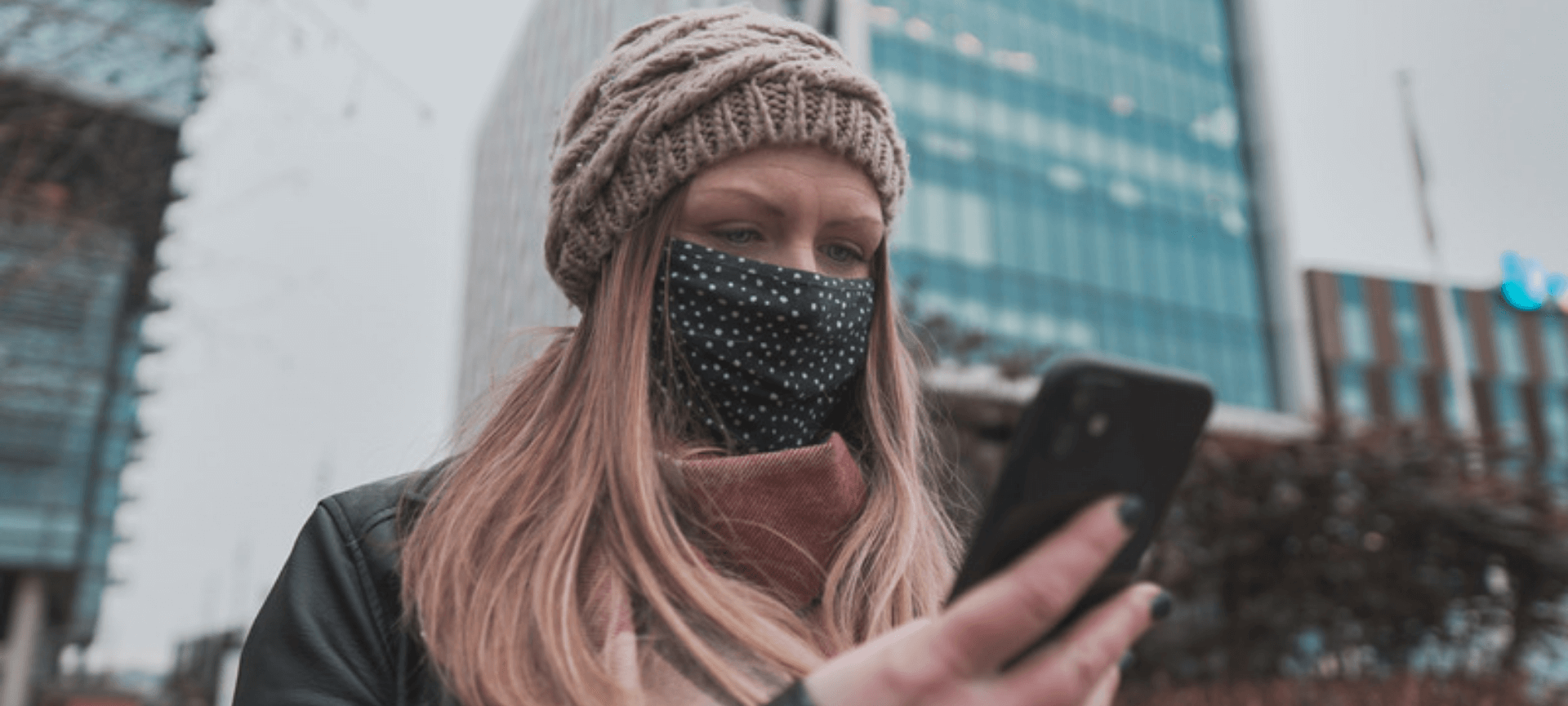 woman wearing face mask and beanie, looking at her phone