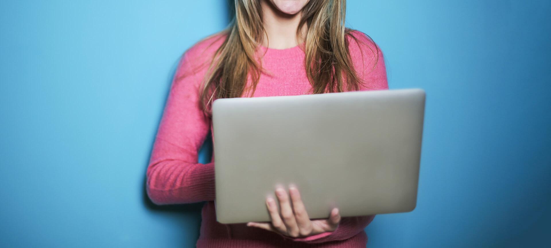 woman in pink top holding laptop with blue background