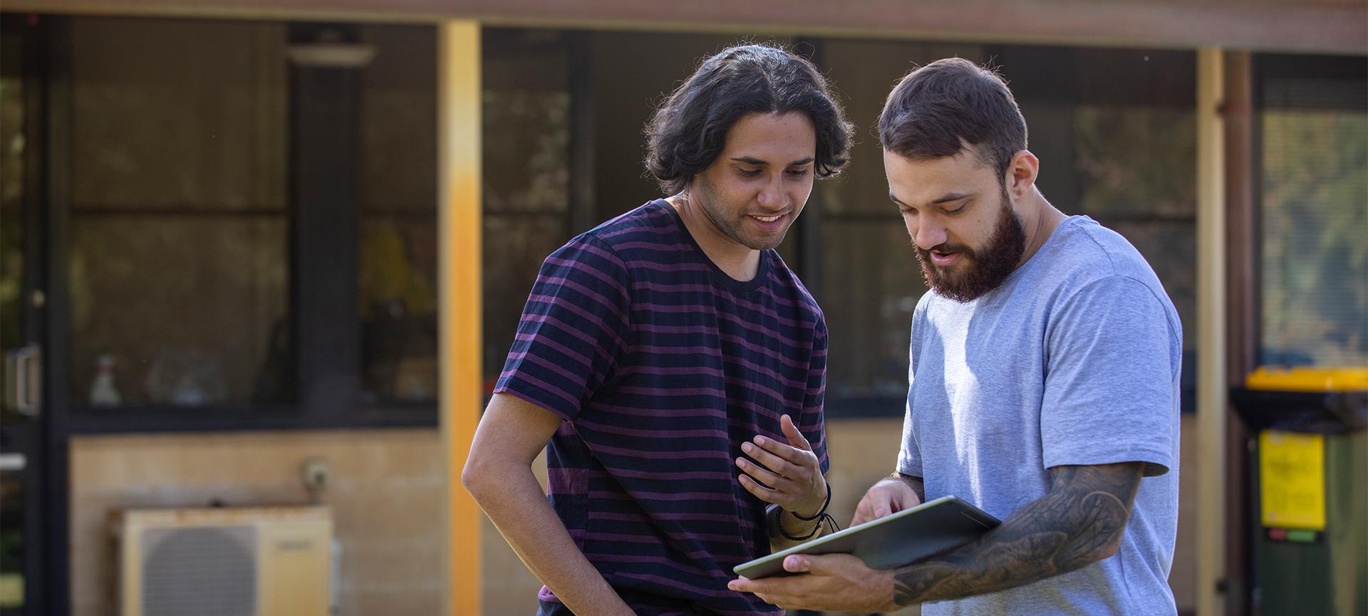 Two men looking standing outside at an ipad