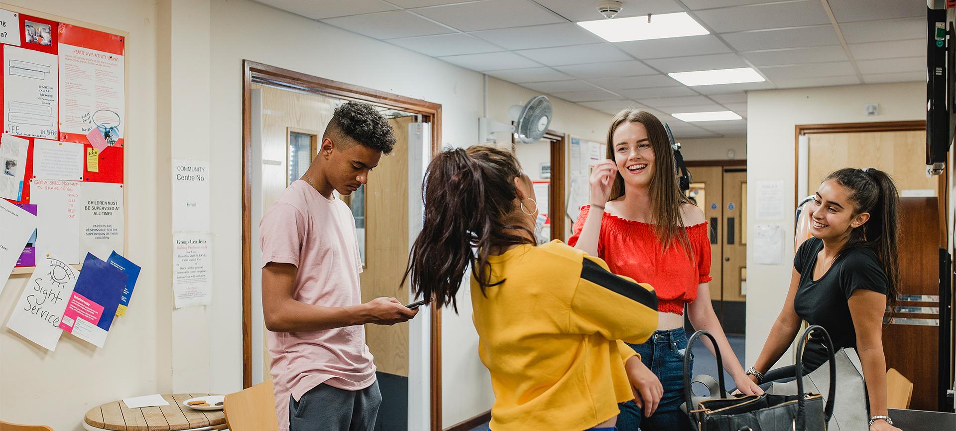 Four teenagers hanging out talking and smiling in a youth centre