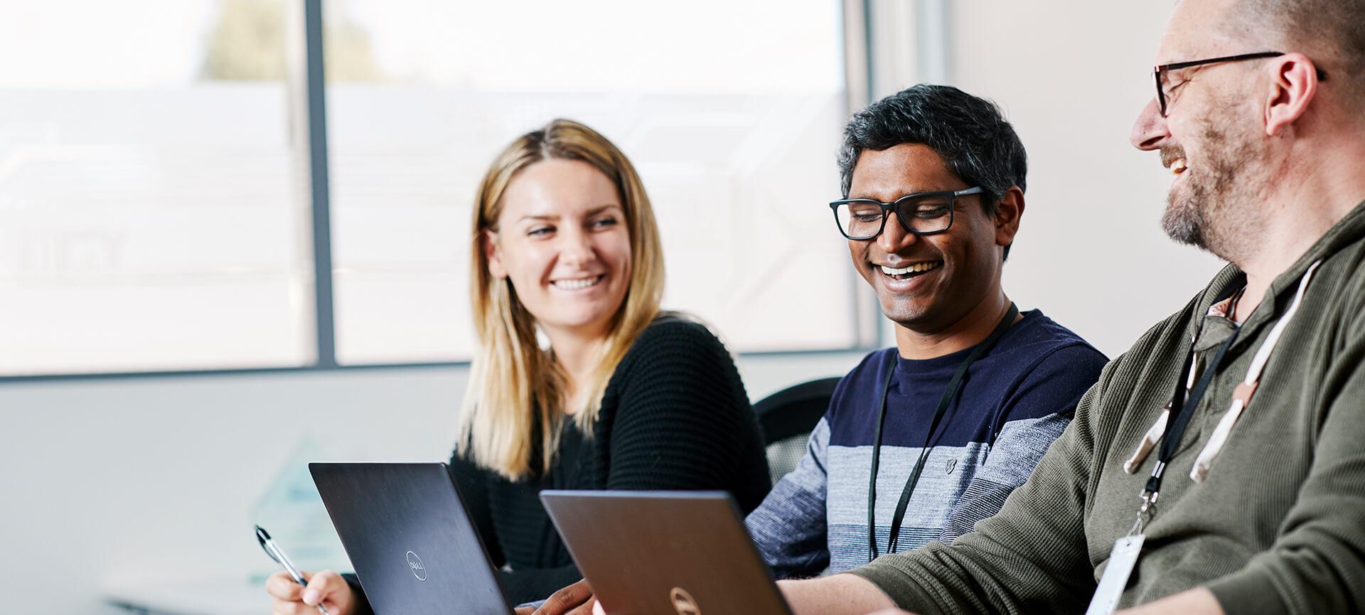 Three workers using laptops and smiling