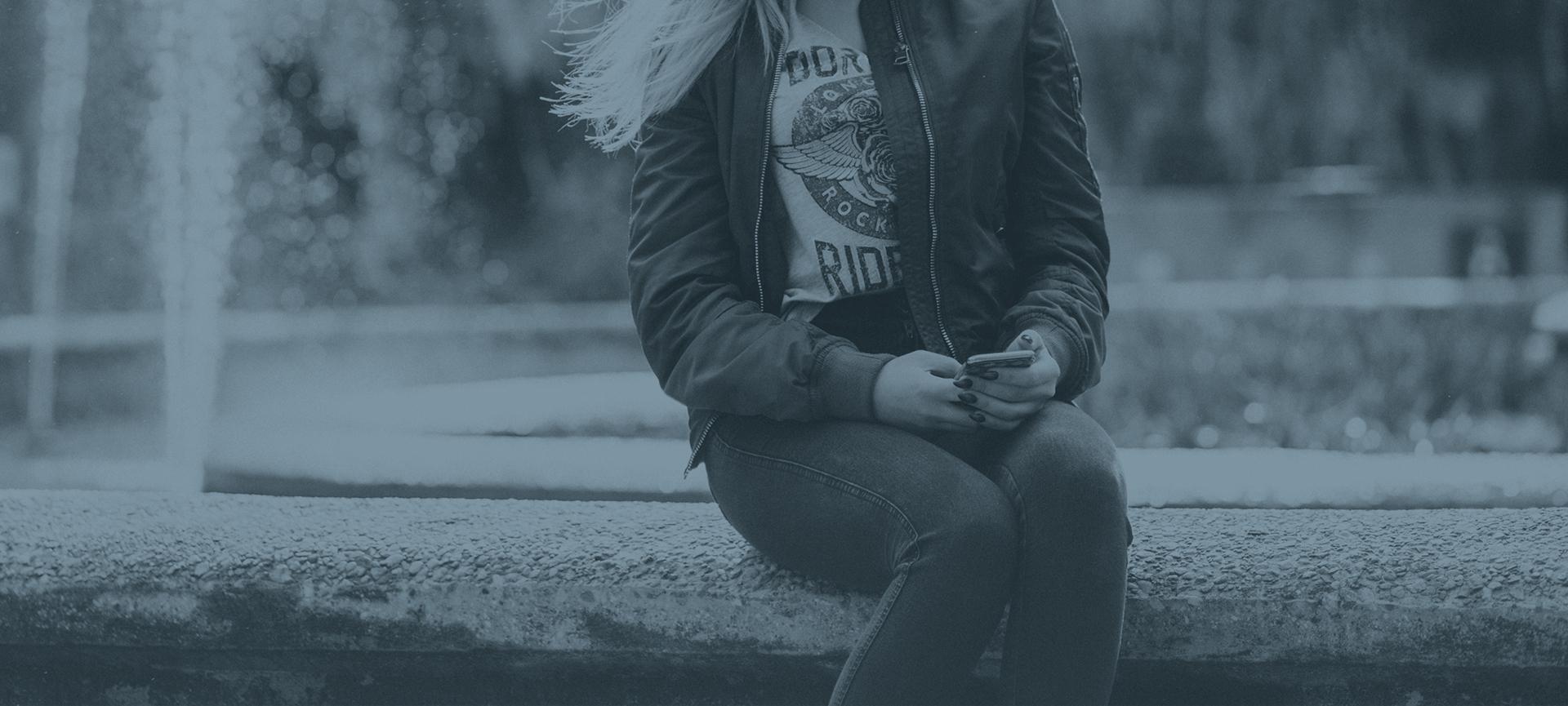 woman sitting on edge of water fountain looking at phone