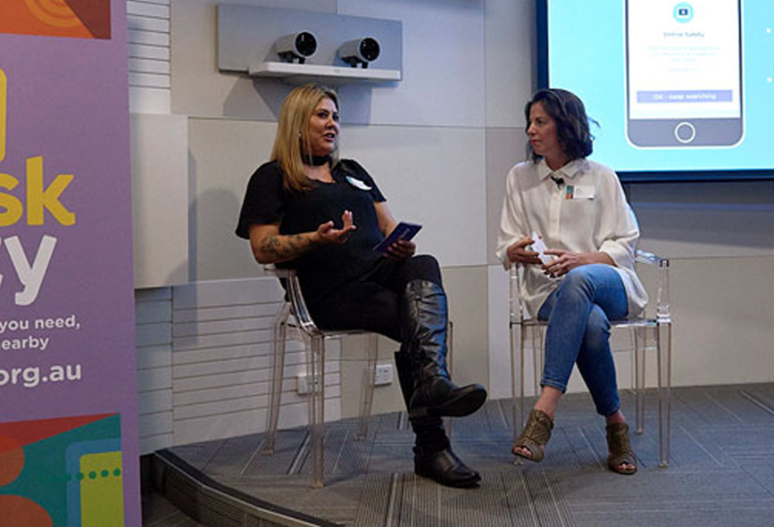 Vicky sitting on stage with woman being interviewed about Ask Izzy