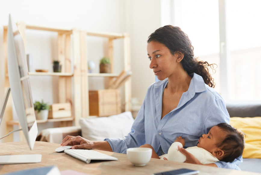 Woman holding her baby whilst working at her desk.