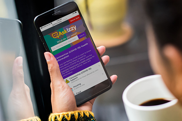 Ask Izzy on mobile screen held by woman with coffee Ask Izzy on mobile screen held by woman with coffee